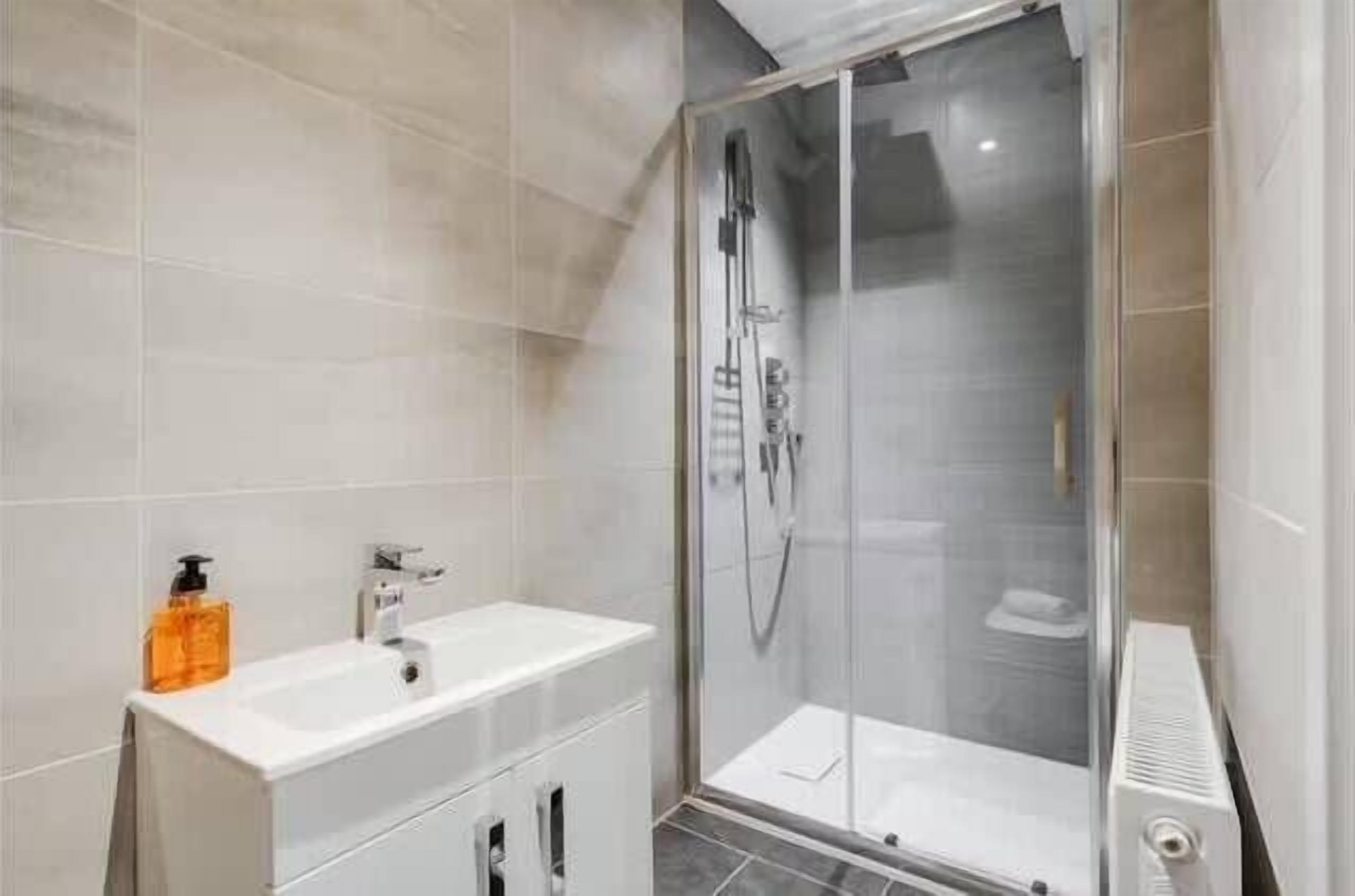 A modern bathroom with a glass-enclosed shower, a white sink with a soap dispenser, and a towel rack.