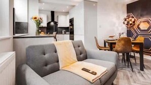 Un salon moderne avec un canapé gris, un coin repas agrémenté d’un motif hexagonal sur le mur, et une cuisine en arrière-plan.
