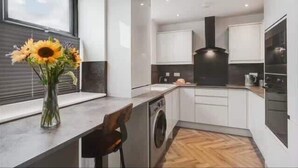 Une cuisine moderne dotée d’un lave-linge intégré, de meubles blancs et d’une grande fenêtre.