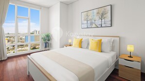 A modern hotel room with a large bed, a nightstand with a lamp, a window with a view of buildings, and a painting on the wall. - Maruva by Kozystay - Taman Sari (Jakarta)