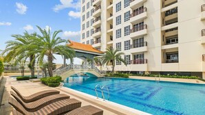 A swimming pool with lounge chairs, a bridge, and a multi-story building with balconies. - Maruva by Kozystay - Taman Sari (Jakarta)
