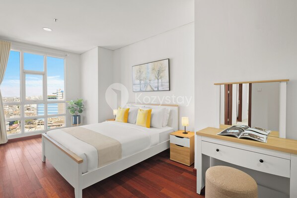 Ein modernes Hotelzimmer mit einem großen Bett, Nachttischen, einem Schreibtisch und Blick auf die Stadt durch große Fenster.