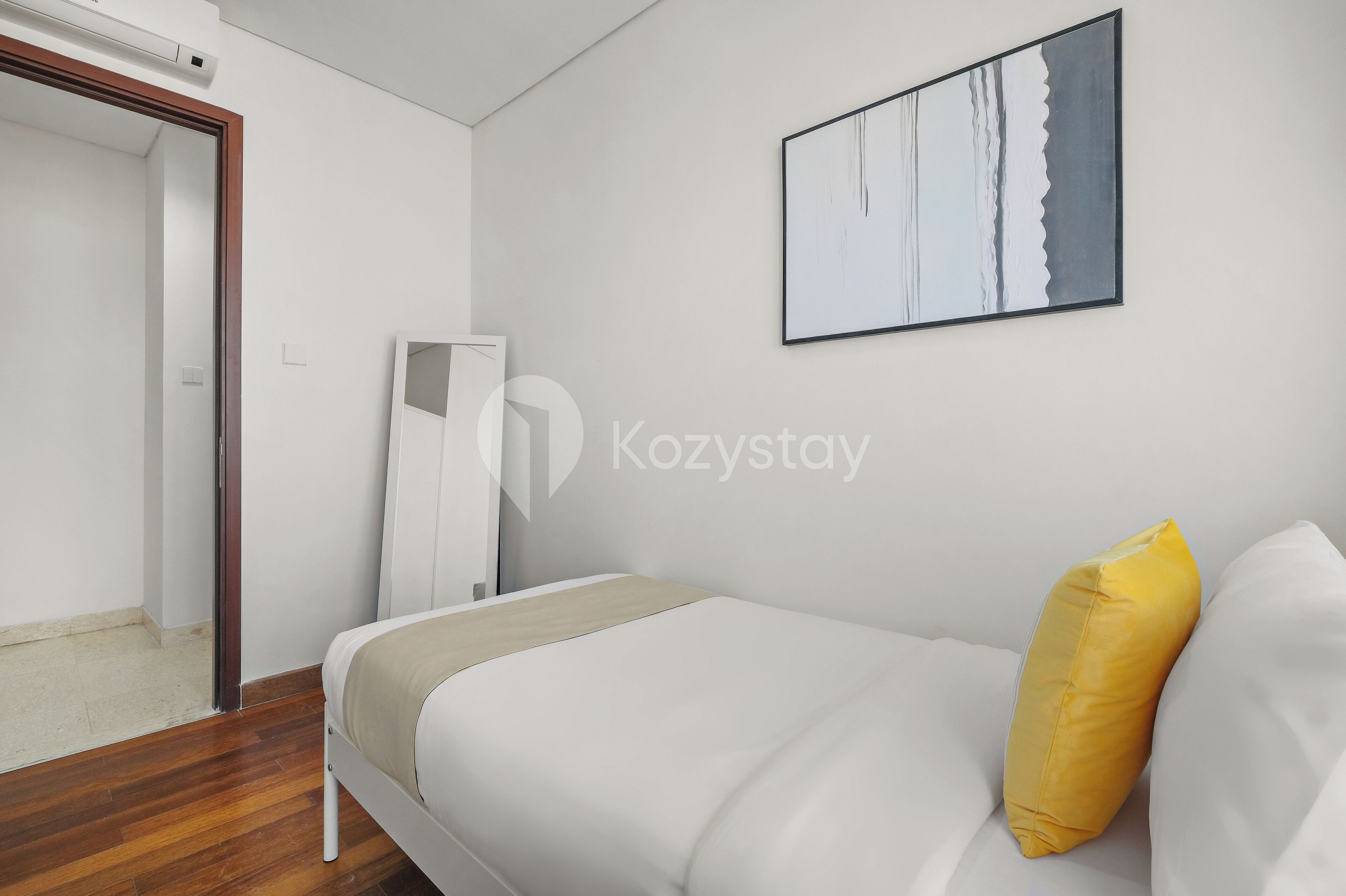 A modern hotel room with a bed, a yellow pillow, a white wall, and a framed artwork.