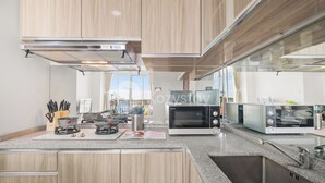 A modern kitchen with wooden cabinets, a built-in microwave, a toaster, and a stainless steel sink. - Maruva by Kozystay - Taman Sari (Jakarta)