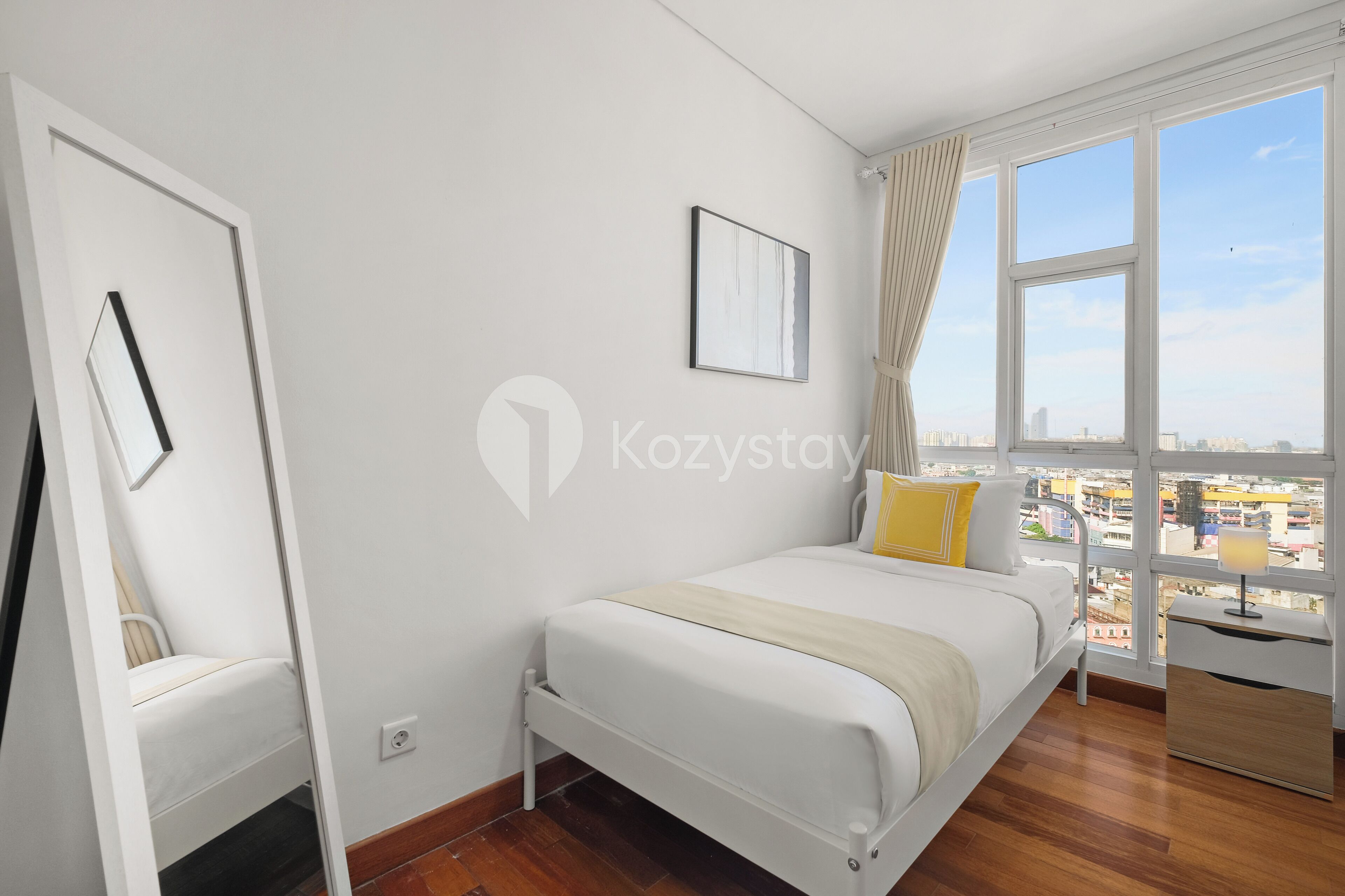 A bedroom with a bed, a nightstand, a window with curtains, and a city view.