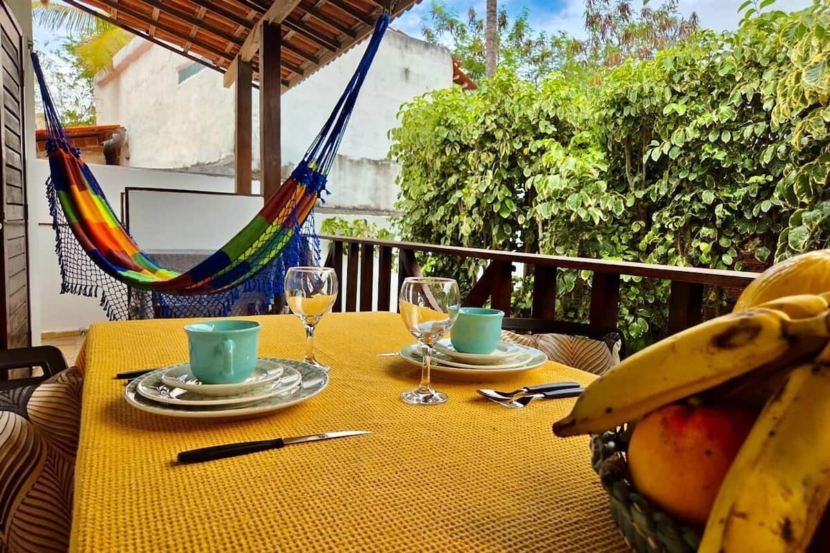 A dining table with a yellow tablecloth, two blue cups, two wine glasses, and a banana on the table.