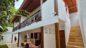 Un edificio de dos pisos con un balcón, una hamaca y una escalera.