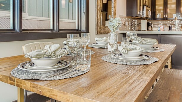 A dining table set with white plates, silverware, and glassware, with a vase of flowers and a candle on the table. - Tranquil Blackstone Getaway 3 Bedroom Townhouse (Park City)