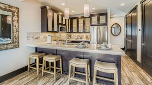 A modern kitchen with dark cabinets, stainless steel appliances, and a central island with stools. - Tranquil Blackstone Getaway 3 Bedroom Townhouse (Park City)