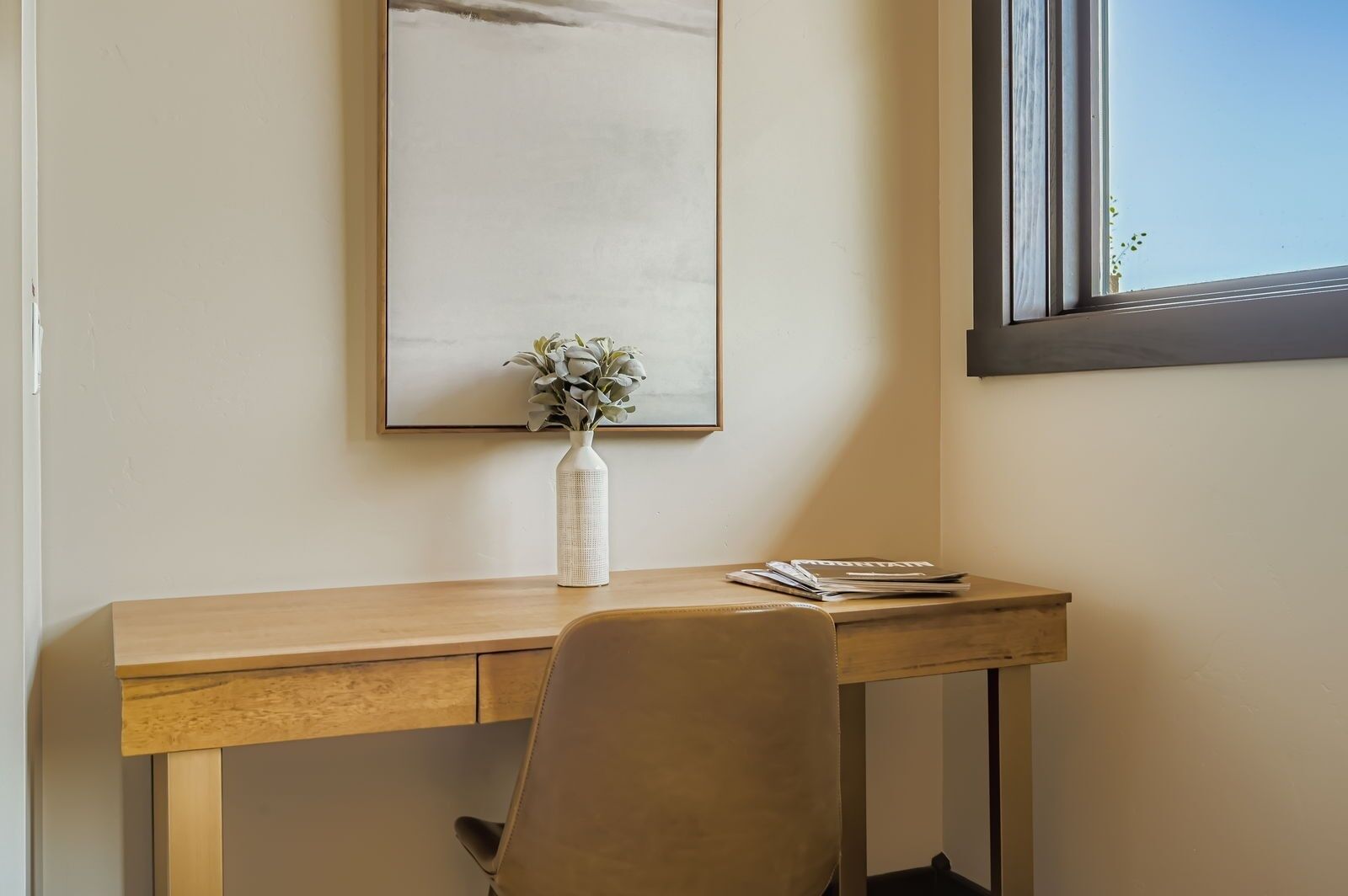 Un espacio de trabajo con un escritorio de madera, una silla, un florero con flores y un cuadro en la pared.
