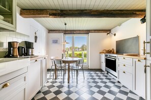 Una cocina con armarios blancos, piso a cuadros, una mesa de comedor con sillas, una ventana con vistas y una lámpara colgante.
