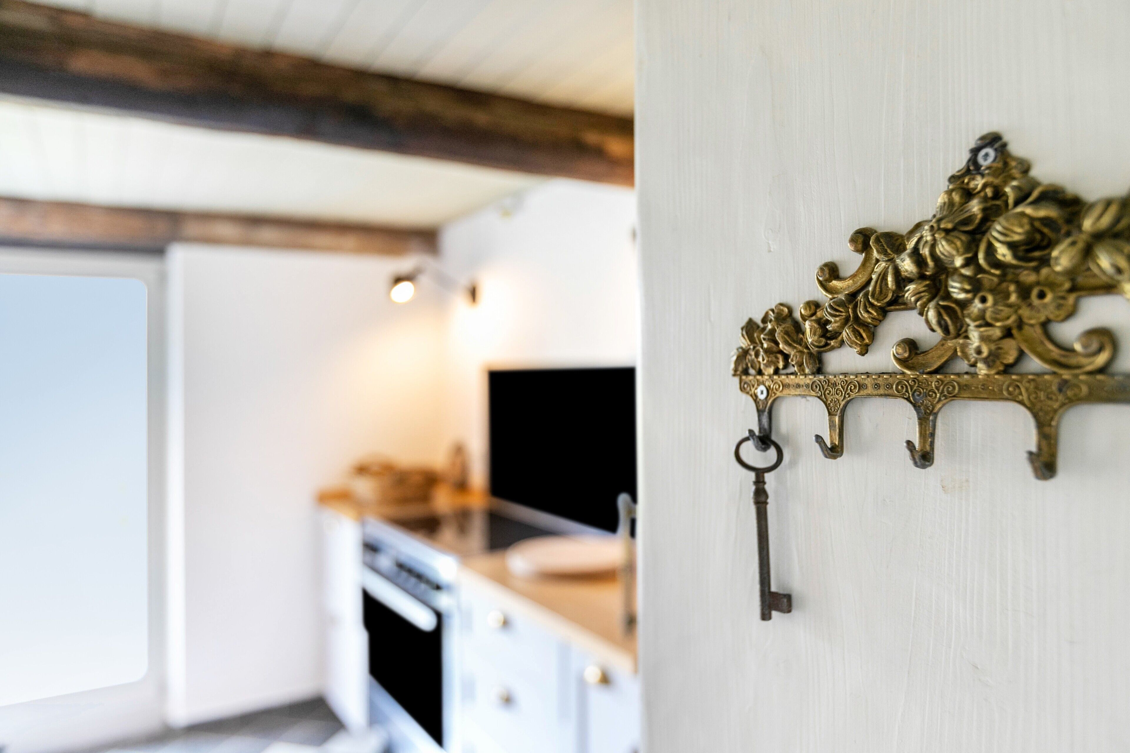 Une cuisine avec des armoires blanches, un plafond en bois et un porte-clés en laiton fixé au mur.