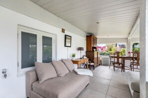 Un'area patio coperta con un divano color beige, un tavolo da pranzo in legno, sedie e un armadietto.