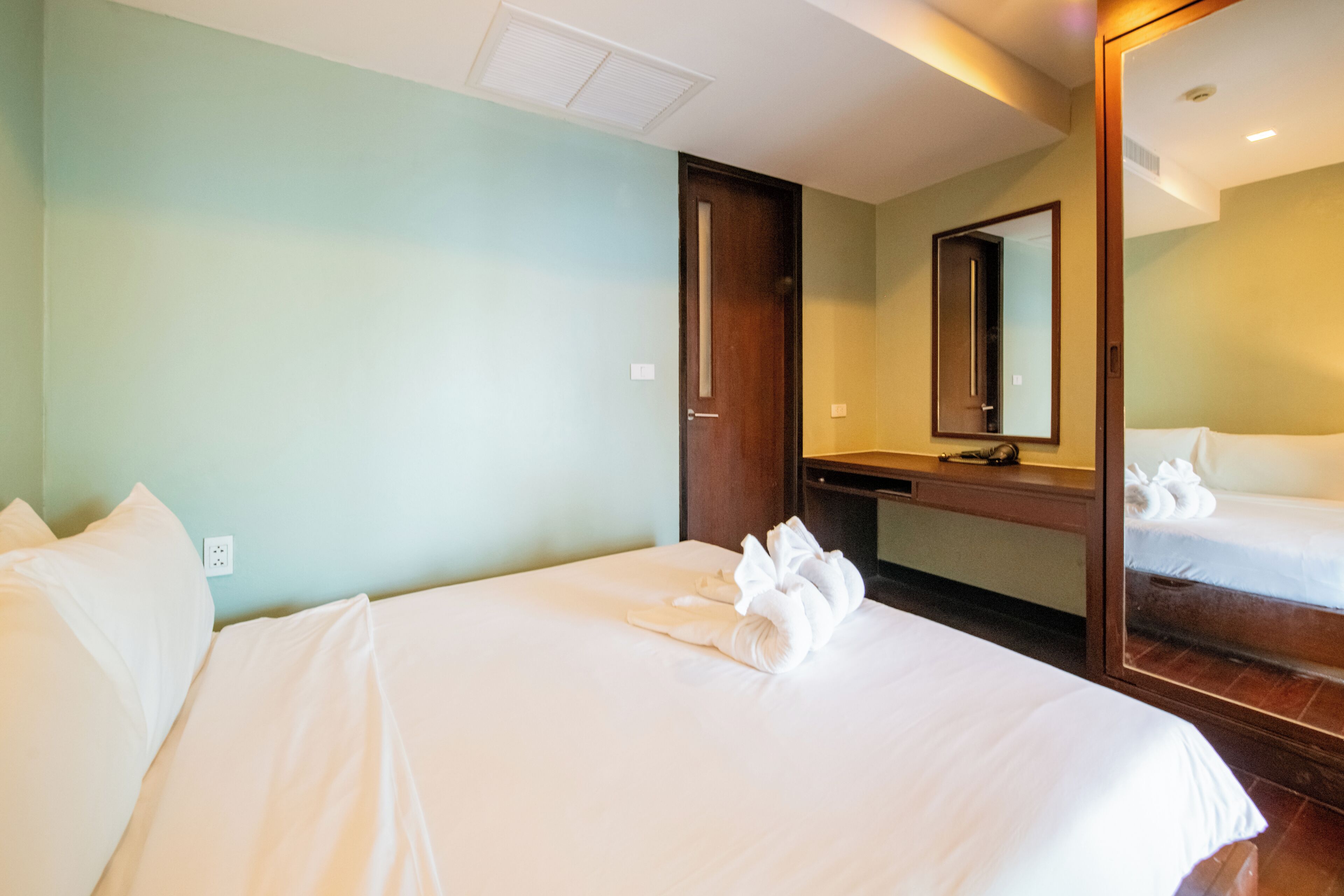 A hotel room with a bed, a desk, a mirror, and a door.