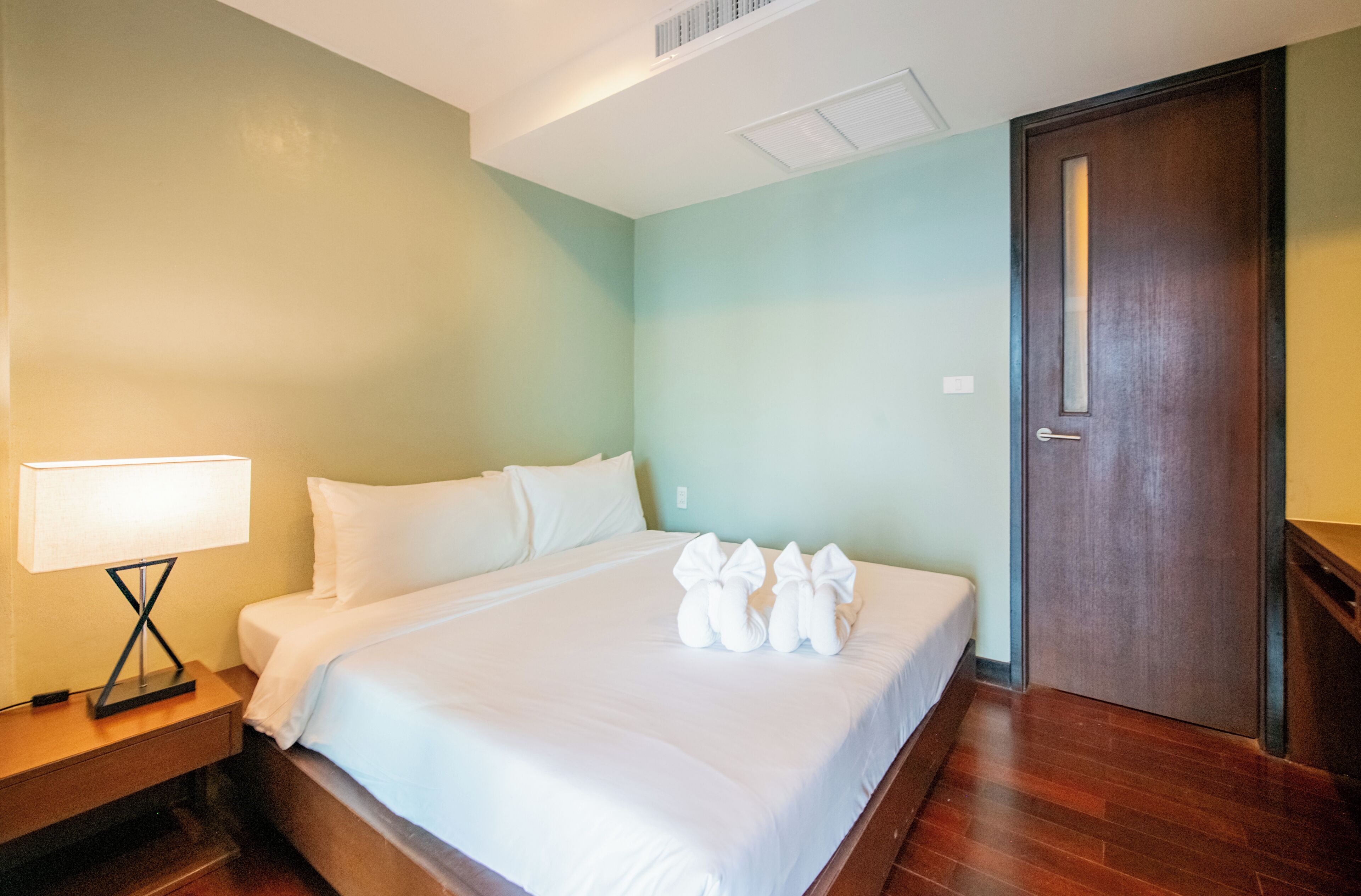 A hotel room with a bed, a nightstand, a lamp, and a door.