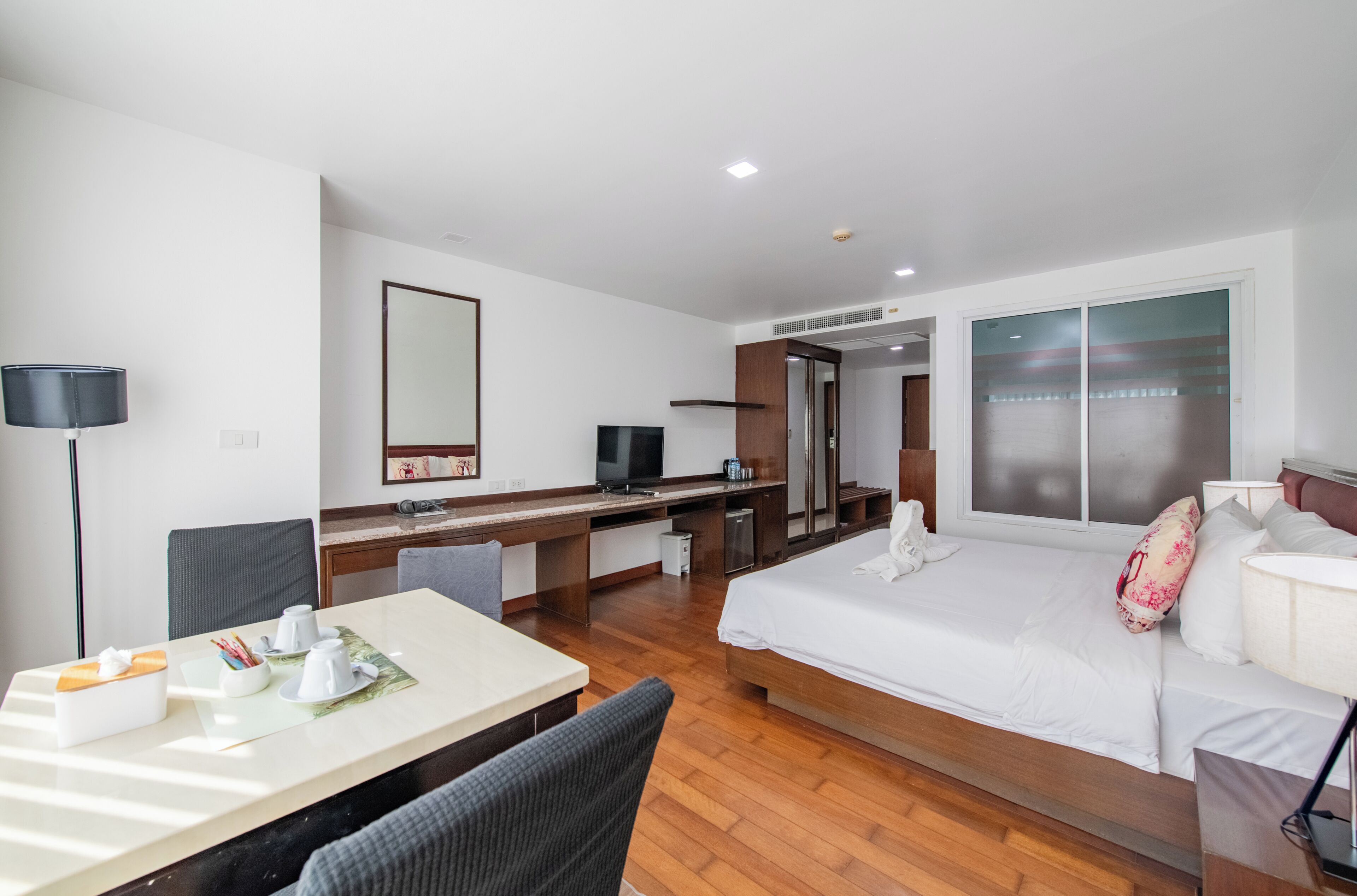 A hotel room with a bed, a desk with a chair, a TV, a mirror, and a wardrobe.