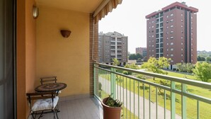 A balcony with a table and chair, a potted plant, and a view of a tall building. - GuestHost - Milano Chiesa Rossa Comfy Apartment (Milan)