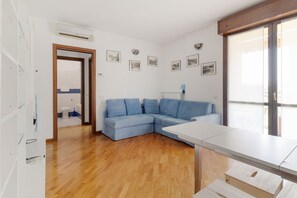 A modern living room with a wooden floor, a blue sectional sofa, a white table, and a large window.