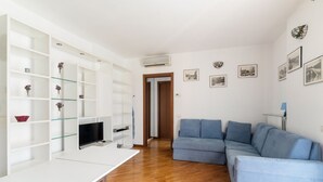 A modern living room with a sofa, TV, and shelves. - GuestHost - Milano Chiesa Rossa Comfy Apartment (Milan)