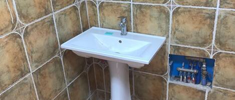 A bathroom with a white pedestal sink, tiled walls, and a wooden floor.