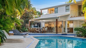 A modern house with a pool, outdoor dining area, and lush tropical vegetation.
