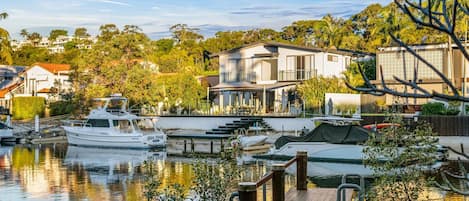 A marina with boats docked, a modern house with a balcony overlooking the water, and a wooden deck in the foreground.