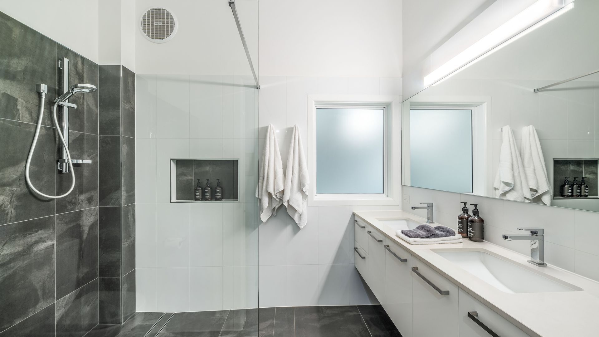 Une salle de bain moderne avec une douche, un grand miroir et un meuble-lavabo doté d’un évier et d’un porte-serviettes.