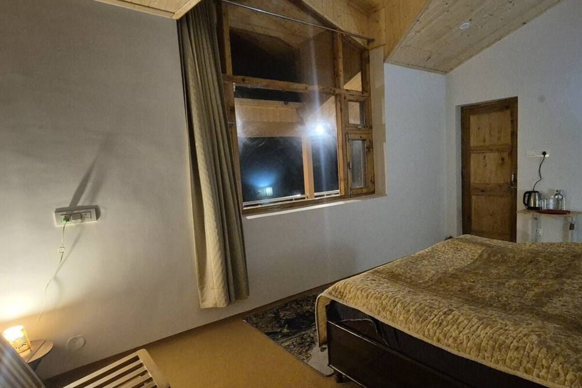 A bedroom with a bed, a window with curtains, a radiator, and a wall socket.
