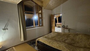 Un dormitorio con cama, una ventana con cortinas, una mesita de noche y un tocador.