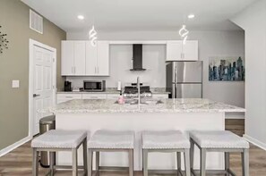 A modern kitchen with white cabinets, a central island with bar stools, stainless steel appliances, and pendant lighting. - Family Friendly 4bed 3bath house in Pittsburgh Walk to the Overlook (Pittsburgh)