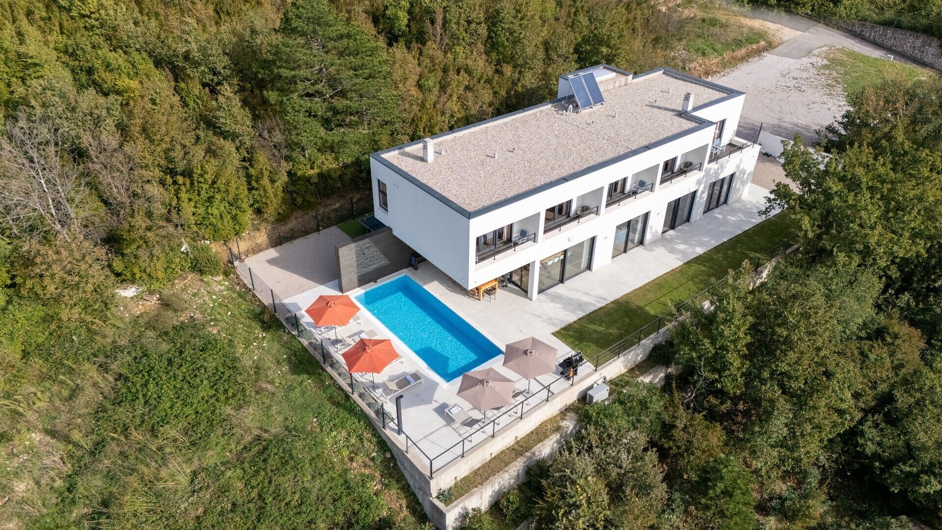 Una casa moderna de dos pisos con un panel solar en la azotea, una piscina y mobiliario de exterior.