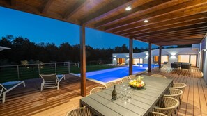 Un espace extérieur abrité comprenant une piscine, des chaises longues et une table à manger avec une bouteille et des verres.