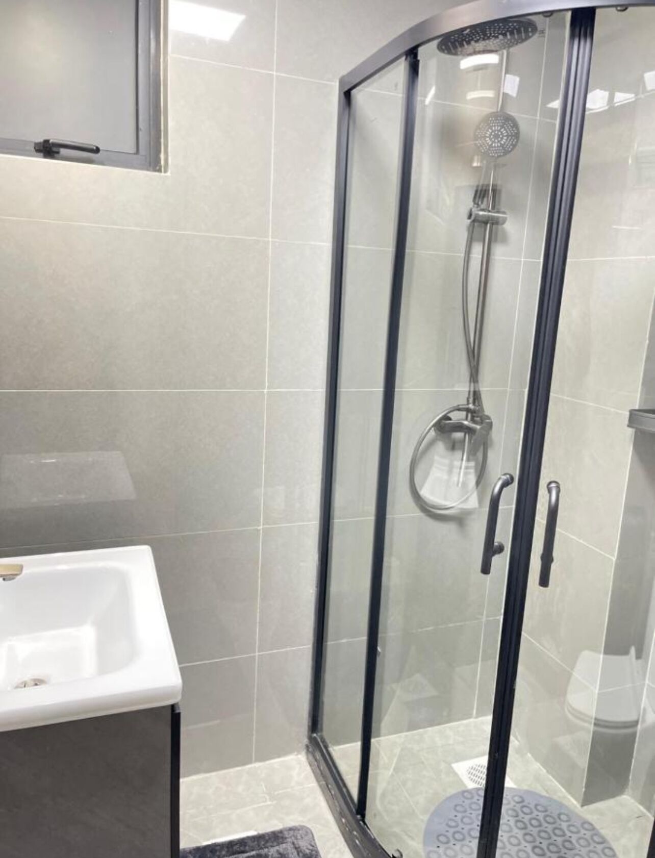 A glass-enclosed shower with a handheld showerhead and a handheld basin.
