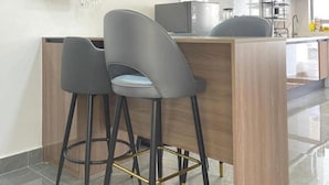 Moderni keittiö, jossa on keskeinen saareke, baarituolit, riippuvalaisimet ja puukehikoiset kaapit.