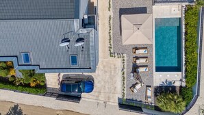 Vue aérienne d’un bâtiment moderne doté d’une piscine sur le toit, d’un espace de détente extérieur et d’une voiture garée dans un espace abrité.
