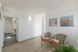 A spacious room with a wooden floor, two wicker chairs with cushions, a wall-mounted light, and two framed pictures. - Casa Vacacional 'Callao 1' con Vista al Mar, Wi-Fi y Aire Acondicionado (Playa Quemada)