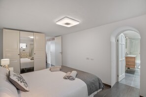A bedroom with a bed, a bedside table, a mirror, a wardrobe, and an arched doorway leading to a bathroom. - Holiday Home 'Callao 2' with Sea View, Wi-Fi and Air Conditioning (Playa Quemada)