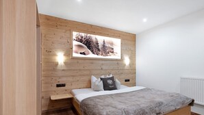 A bedroom with a wooden headboard, a bed with a gray blanket, a mounted picture of a snowy landscape, and two wall-mounted lights. - Holiday Home 'Anton' with Mountain View, Private Terrace and Wi-Fi (Gerlosberg)