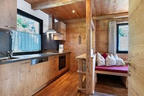 Un intérieur en bois comprenant une cuisine, un coin repas avec un banc et une fenêtre avec des rideaux.