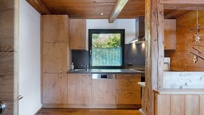 A modern kitchen with wooden cabinets, a built-in dishwasher, and a window with a view of greenery. - Holiday Home 'Anton' with Mountain View, Private Terrace and Wi-Fi (Gerlosberg)