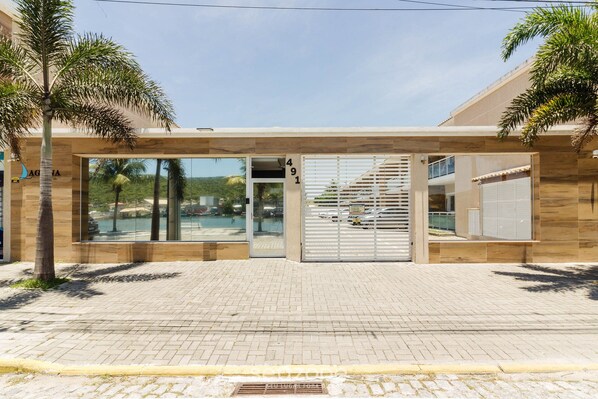 Uma fachada moderna de edifício com porta de vidro, número do endereço visível e escadaria que leva a um andar superior.
