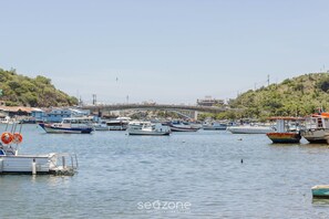 Uma marina com barcos atracados, uma ponte ao fundo e uma paisagem montanhosa.