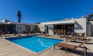 A swimming pool with lounge chairs and a bar area. - Condominium on the Edge of the Cabo Frio Channel - CFR (Cabo Frio)