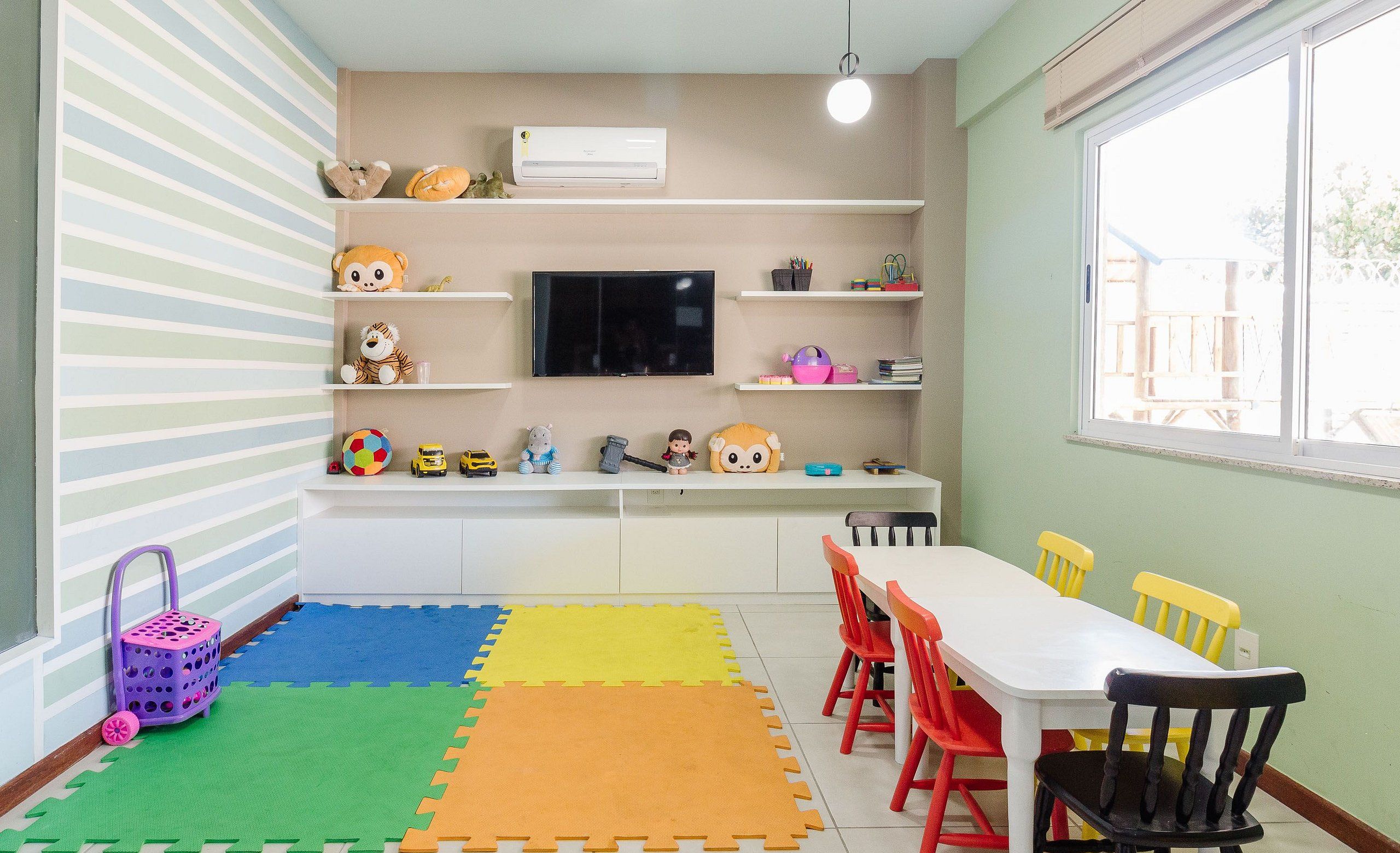 A children's playroom with a white table, colorful chairs, and a play mat.