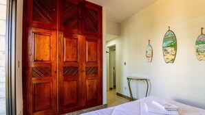 A bedroom with a bed, a wooden wardrobe, and three surfboard decorations on the wall. - Beautiful apt W/suite 300m From Forte Beach Bfc301 (Cabo Frio)