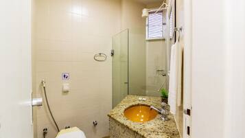 Un baño con lavamanos de granito, cabina de ducha con mampara de vidrio y un inodoro.