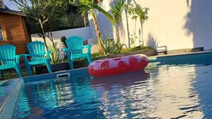 Une piscine à l’eau d’un bleu cristallin, entourée de chaises vertes et d’un flotteur gonflable rouge.