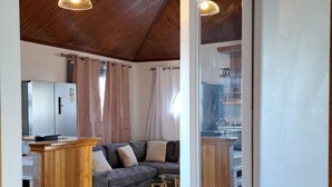Un vaste espace de vie doté d’un plafond en bois, d’un ensemble de canapés et d’une cuisine visible à travers une porte ouverte.