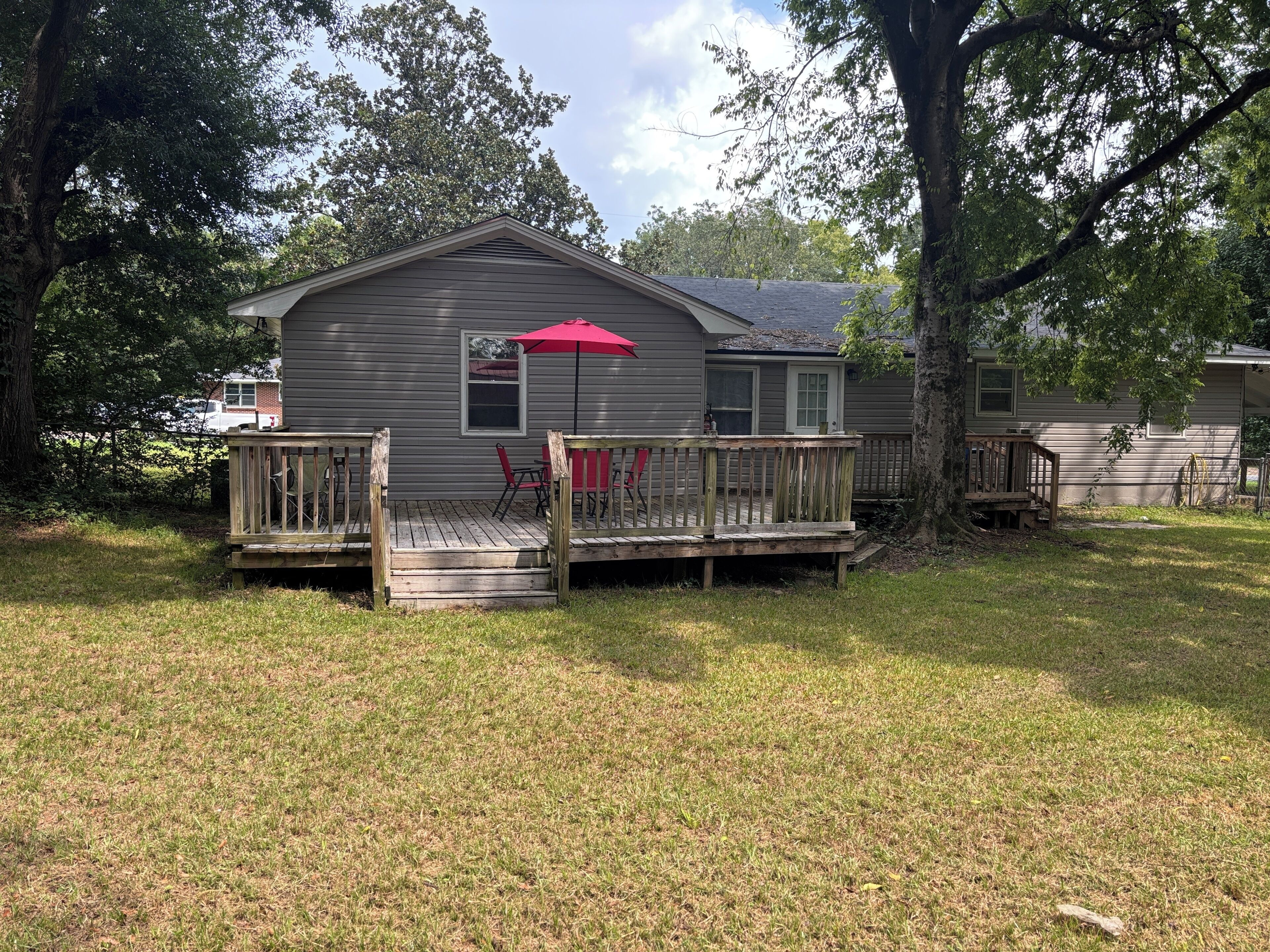 A single-story house with a wooden deck, a red umbrella, and a small patio area with chairs.