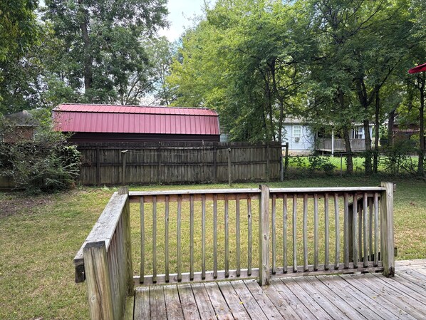 A wooden deck with a metal railing, a red-roofed building, and a wooden fence in a backyard.